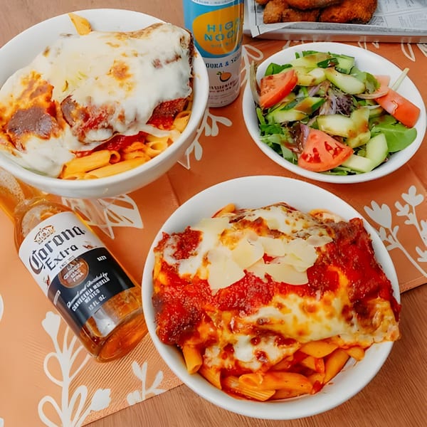 Two bowls of Dox penne pasta with melted cheese and sauce, a side salad, and two beers.