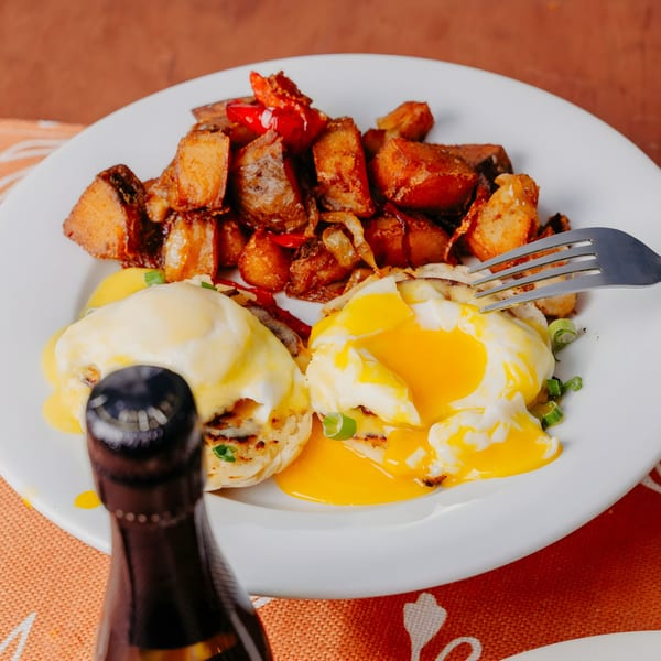 Dox brunch plate with eggs Benedict, home fries, and a bottle of champagne.