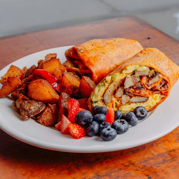 A breakfast burrito with eggs, bacon, and avocado, served with roasted potatoes, strawberries, and blueberries.