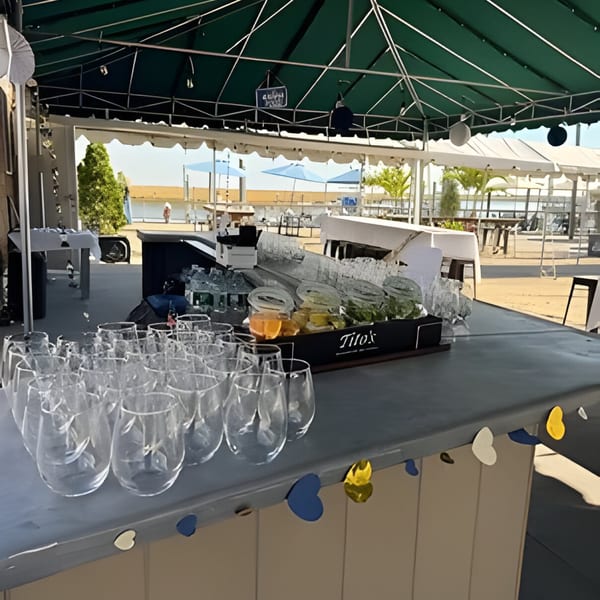 An outdoor bar setup with Dox branding, clear glasses, ice, and citrus under a green canopy.