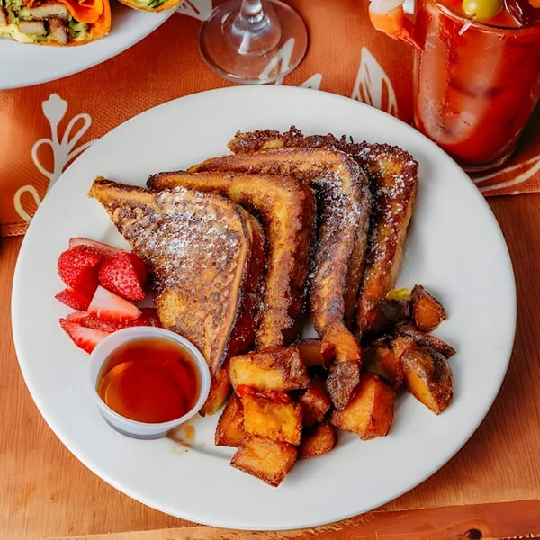 French toast with powdered sugar, strawberries, home fries, and a side of syrup.