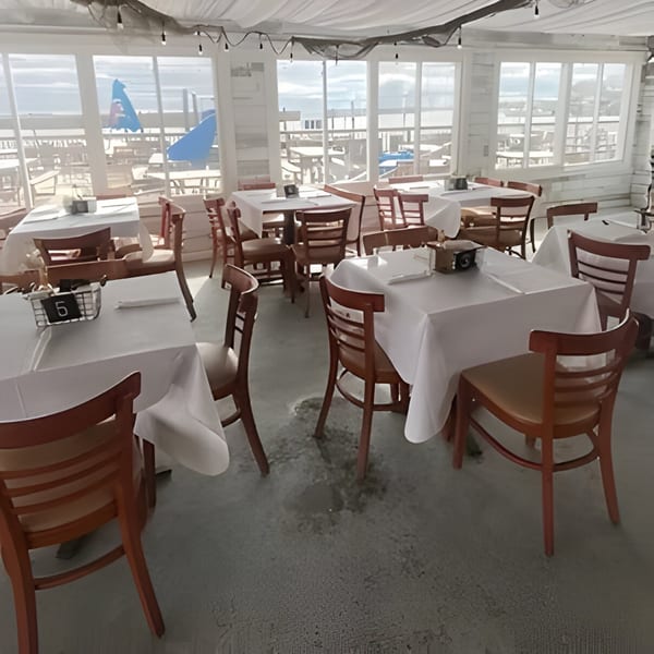 Dox bar's dining area with white tablecloths, wooden chairs, and large windows overlooking the ocean.