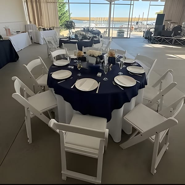 A Dox dining room with round tables set with dark blue tablecloths and white chairs, overlooking water.