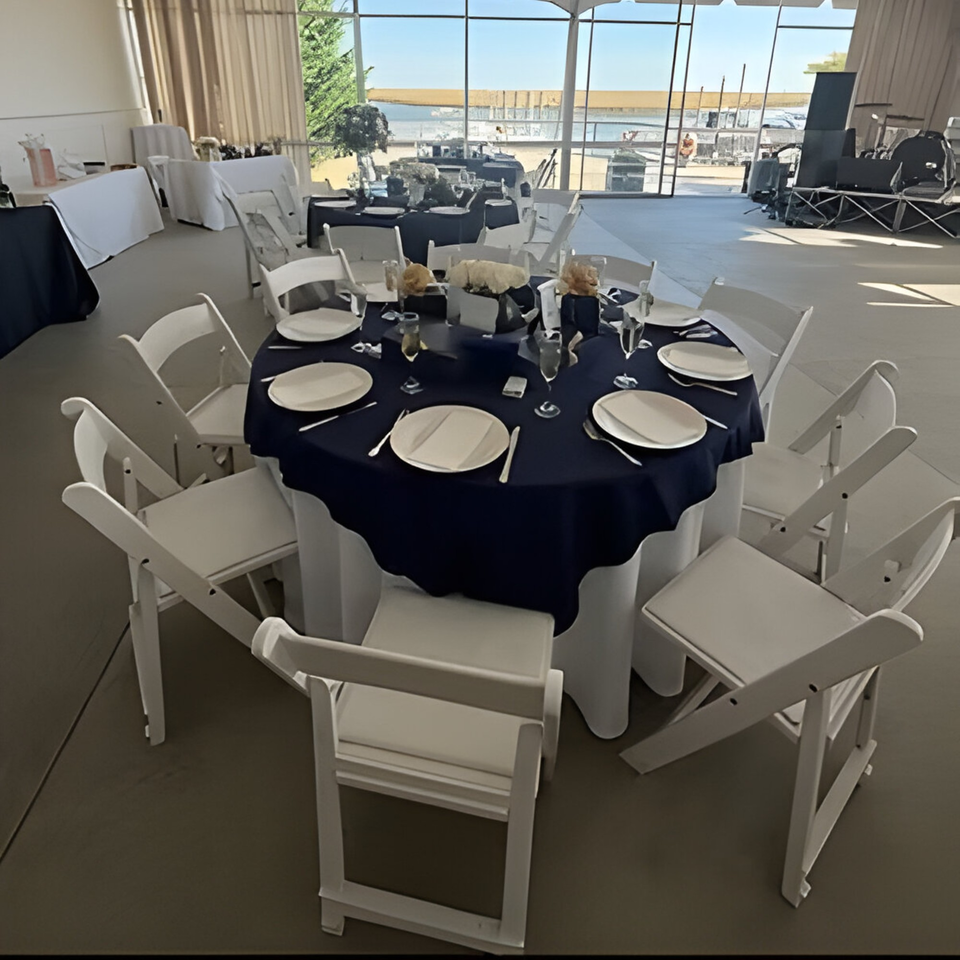 A Dox dining room with round tables set with dark blue tablecloths and white chairs, overlooking water.