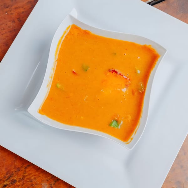 A white square bowl filled with orange Dox bar soup, garnished with green and red pieces.