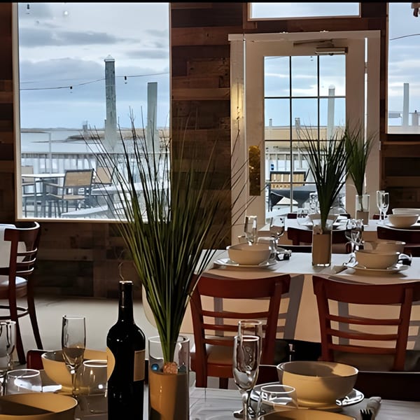 Dox restaurant interior with set tables, wine, and a view of the water and distant structures.