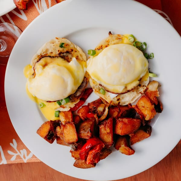 Two eggs benedict with hollandaise sauce and green onions, served with crispy home fries.